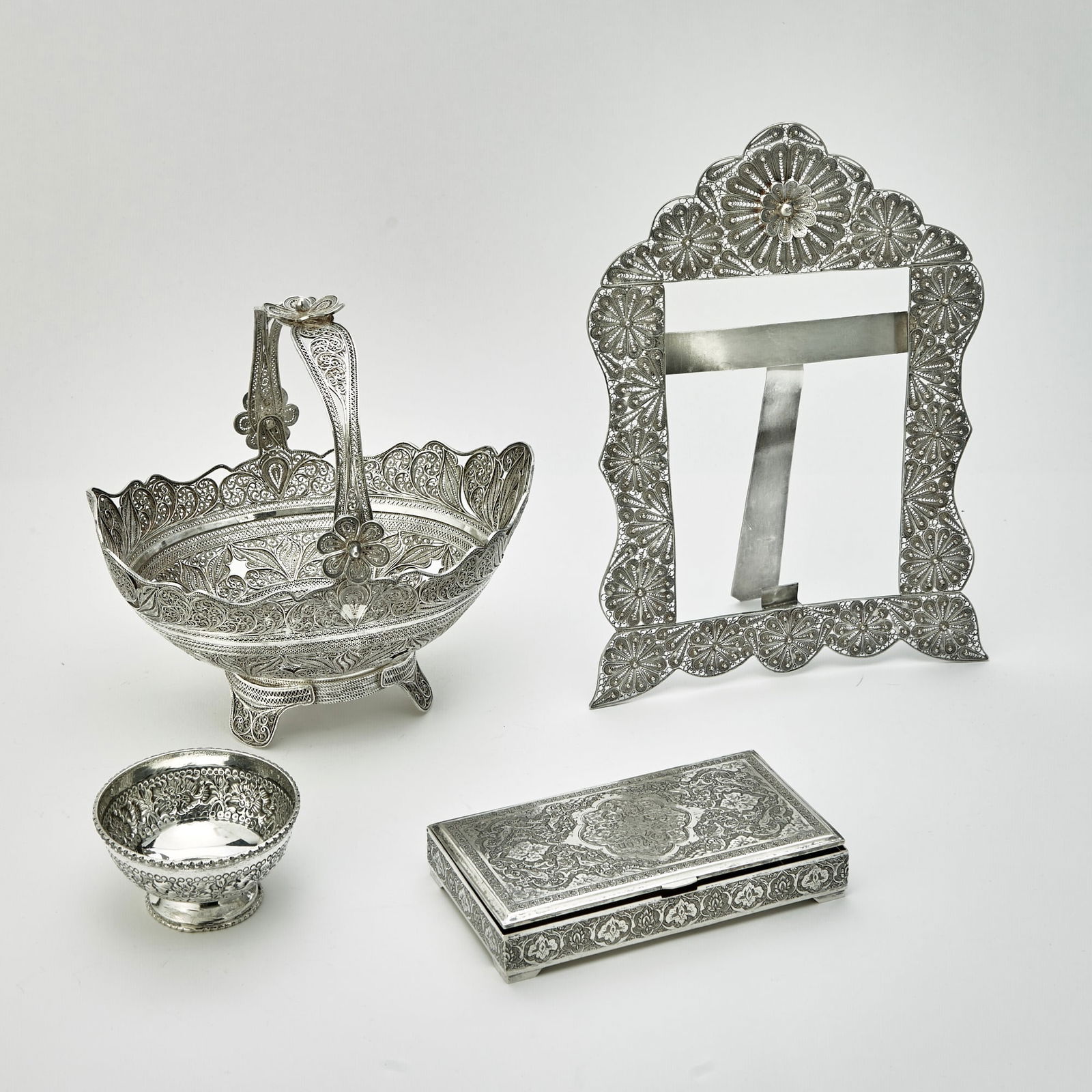 Four Middle Eastern Silver Table Articles: Comprising a photo frame, height 11 inches, width 8 inches; basket height over handle 8 1/4 inches, length 8 1/2 inches; box, length 6 1/4 inches; bowl, height 2 inches, diameter 3 1/2 inches, total a