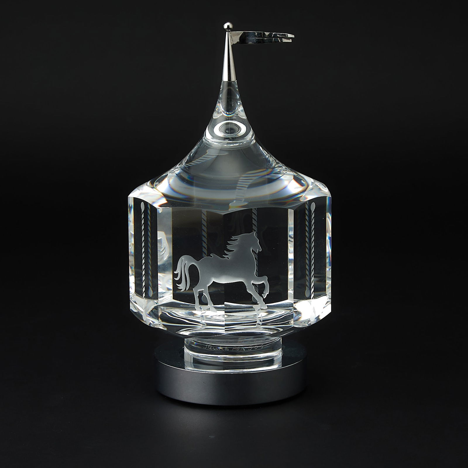 Steuben Glass and Silvered Metal Spinning Carousel: Designed by Peter Aldridge and Jane Osborn-Smith, 1985, from the Major Ornamental Designs Series, cast, cut and engraved glass with silvered metal flag. Height 8 1/4 inches.