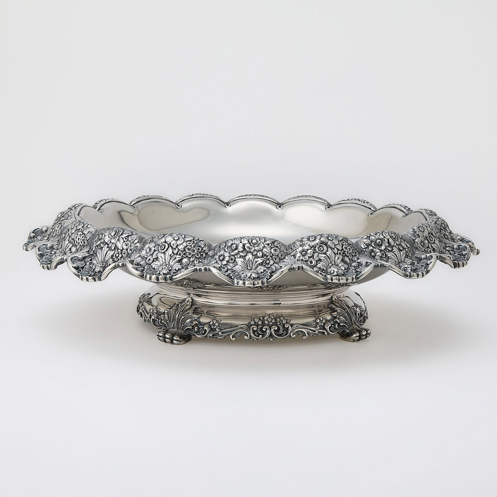 Tiffany & Co. Sterling Silver Centerpiece: 1892-1902 Shaped circular, the rim cast with flowers and foliage, raised on four foliate feet. Height 4 1/8 inches, diameter 17 inches, approximately 61 ounces. Generally good condition overall with