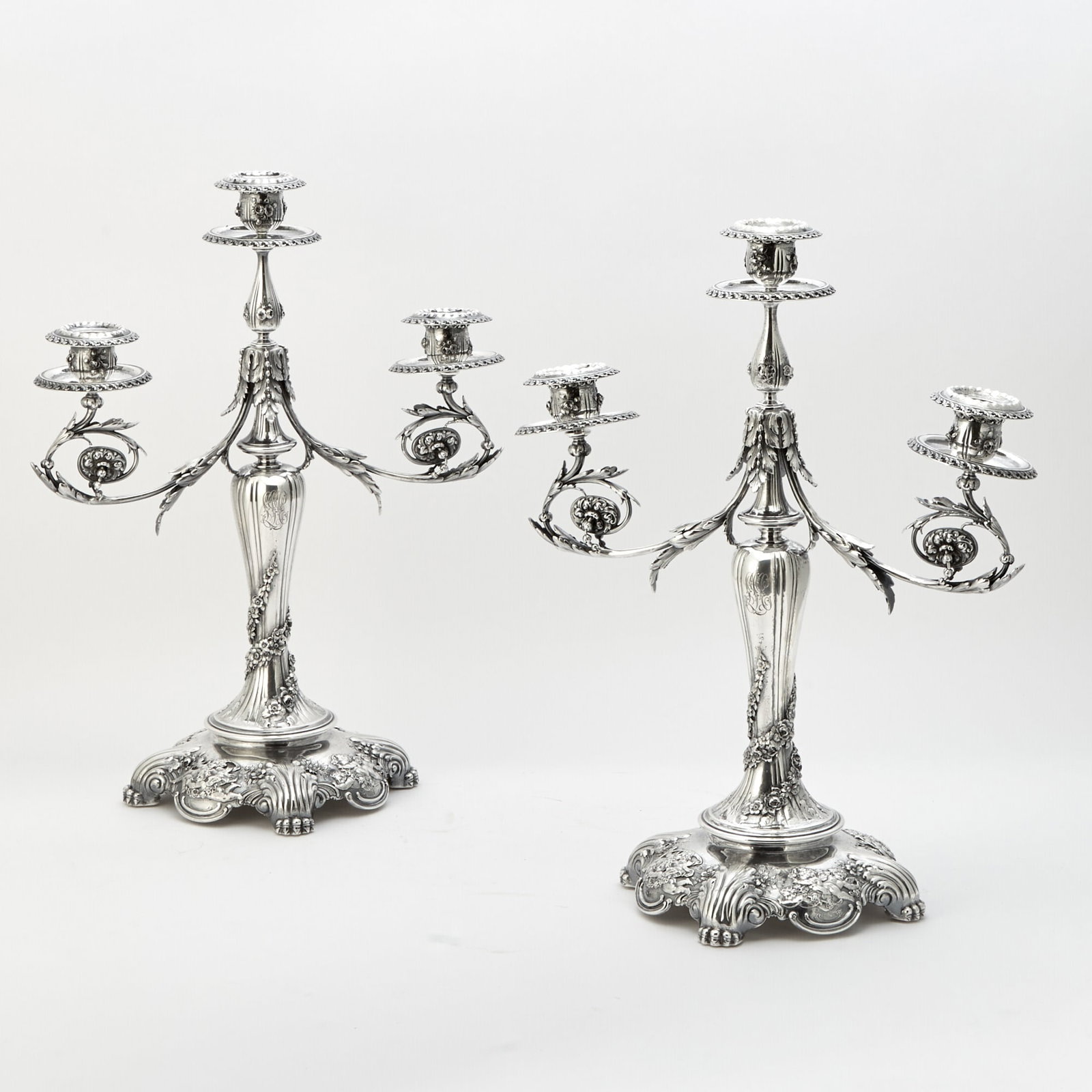 Pair of Tiffany & Co. Sterling Silver Three-Light Candelabra: 1902-1907 Each baluster-form stem with applied spiral floral garland, issuing pair of scrolling foliate branches centering a raised light, on a domed circular base applied with cupids and flowers. Hei