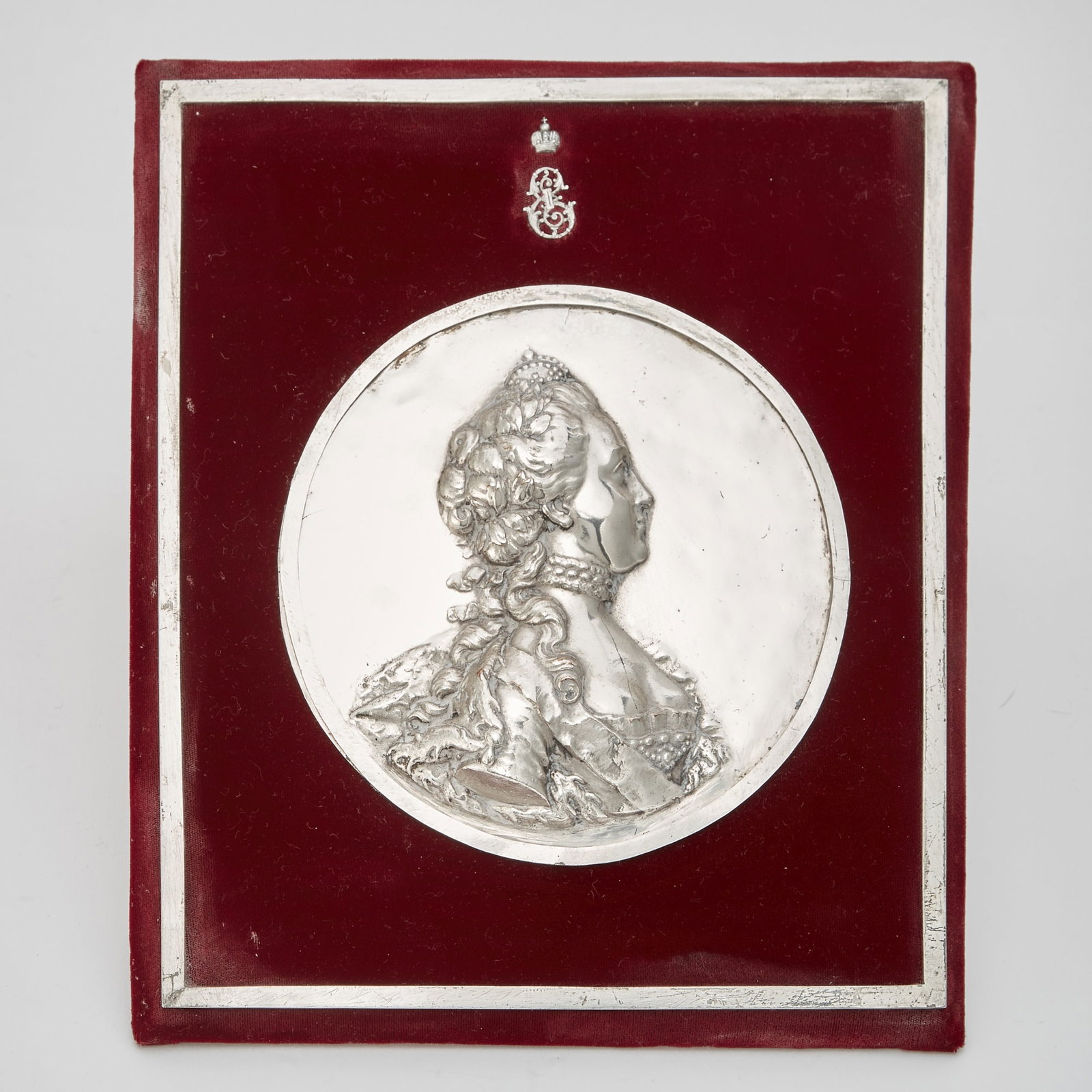 Silver Plated Portrait Medallion of Empress Catherine II: After Jean-Baptiste Nini (Italian, 1717-1786) The Empress depicted half-length in profile, beneath her crowned cypher, on burgundy velvet. Diameter 6 1/2