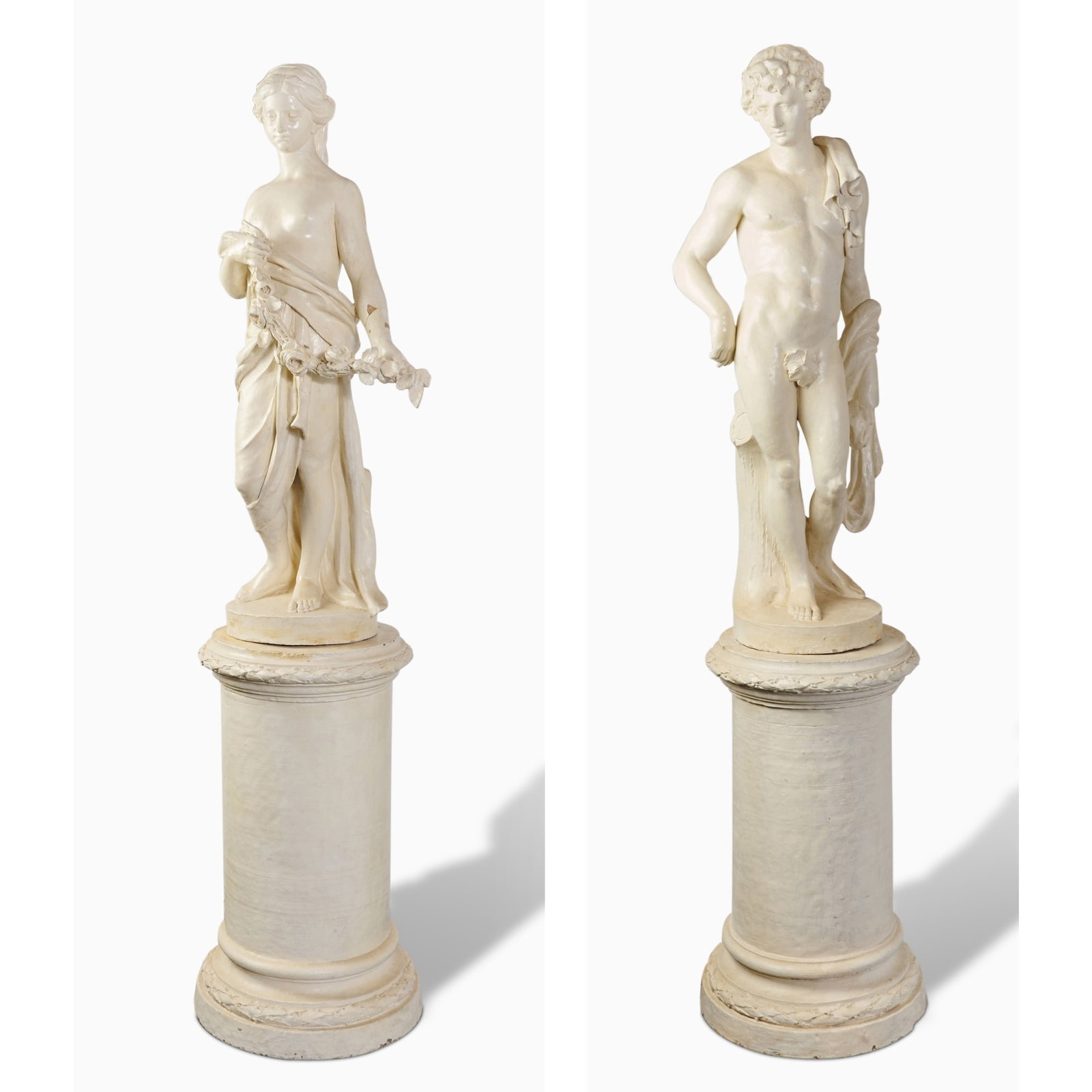 Pair of Italian White-Painted Terracotta Figures of a Maiden and a Youth on Pedestals: 19th Century Each finely carved, the maiden draped in classical robes, holding a floral garland, the youth semi-nude with lion pelt over his shoulder, both on integral circular socle and cylindrical p