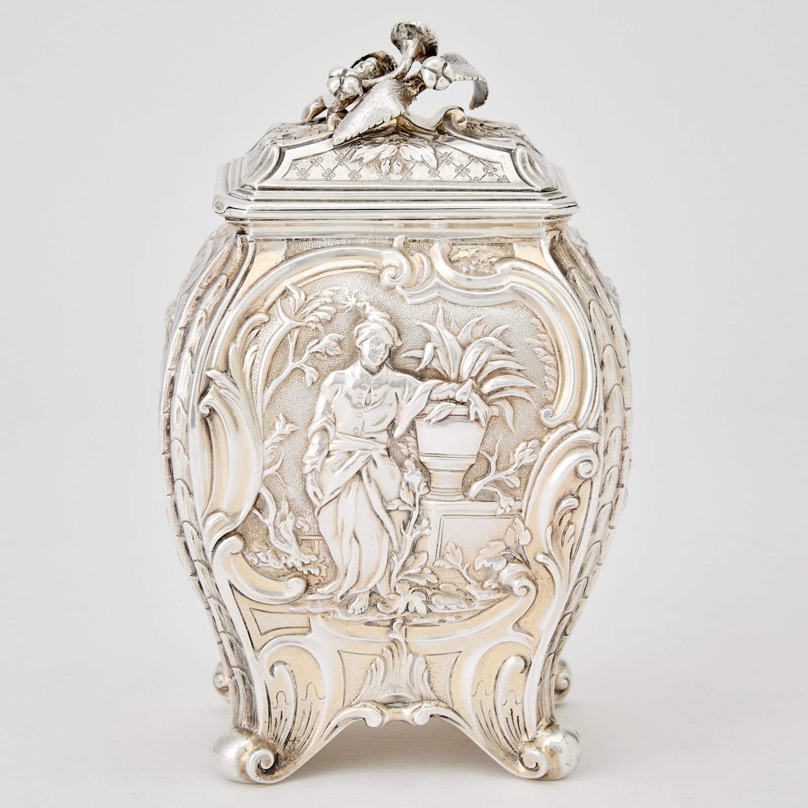 Victorian Sterling Silver Tea Caddy: Robert Garrard, London, 1845 Of bombé-form chased with exotic figures, the cover with tea bud finial, all on scroll feet. Height 6 inches (15.5 cm), width 3 3/4 inches (9.5 cm), approximately 14 