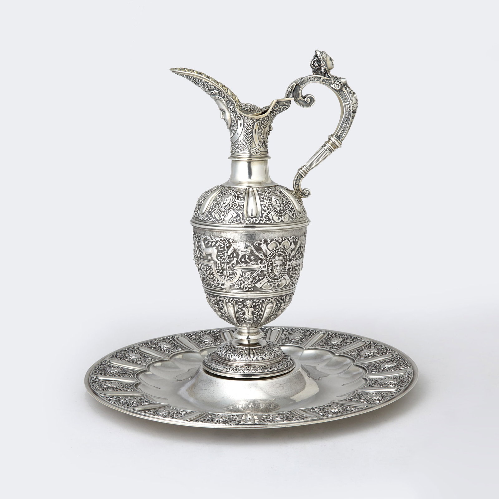 Victorian Sterling Silver "Cellini" Pattern Ewer and Stand: Smith, Nicholson & Co., London, 1874 Each with panels of masks, the ewer with band with rams and deer, the handle with a mask thumbpiece. Height of ewer 11 3/4 inches (30 cm), diameter of stand 12