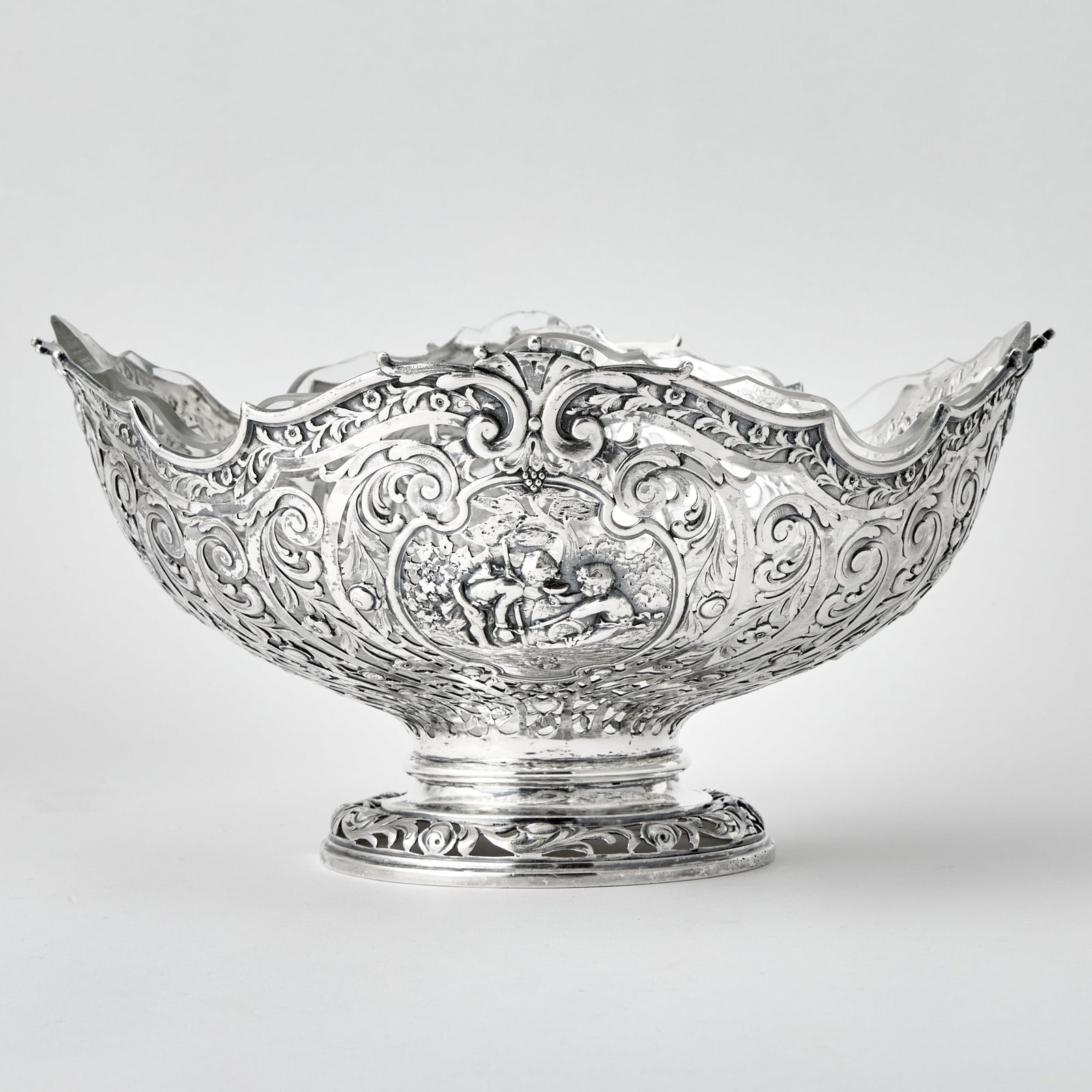 Continental Silver and Glass Centerpiece Bowl: Early 20th century Circular with foliate pierced body centering two figural cartouches, on a domed circular foot. Height 6 inches (15.2 cm), diameter 11 1/2 inches (29 cm), approximately 27 ounces, we