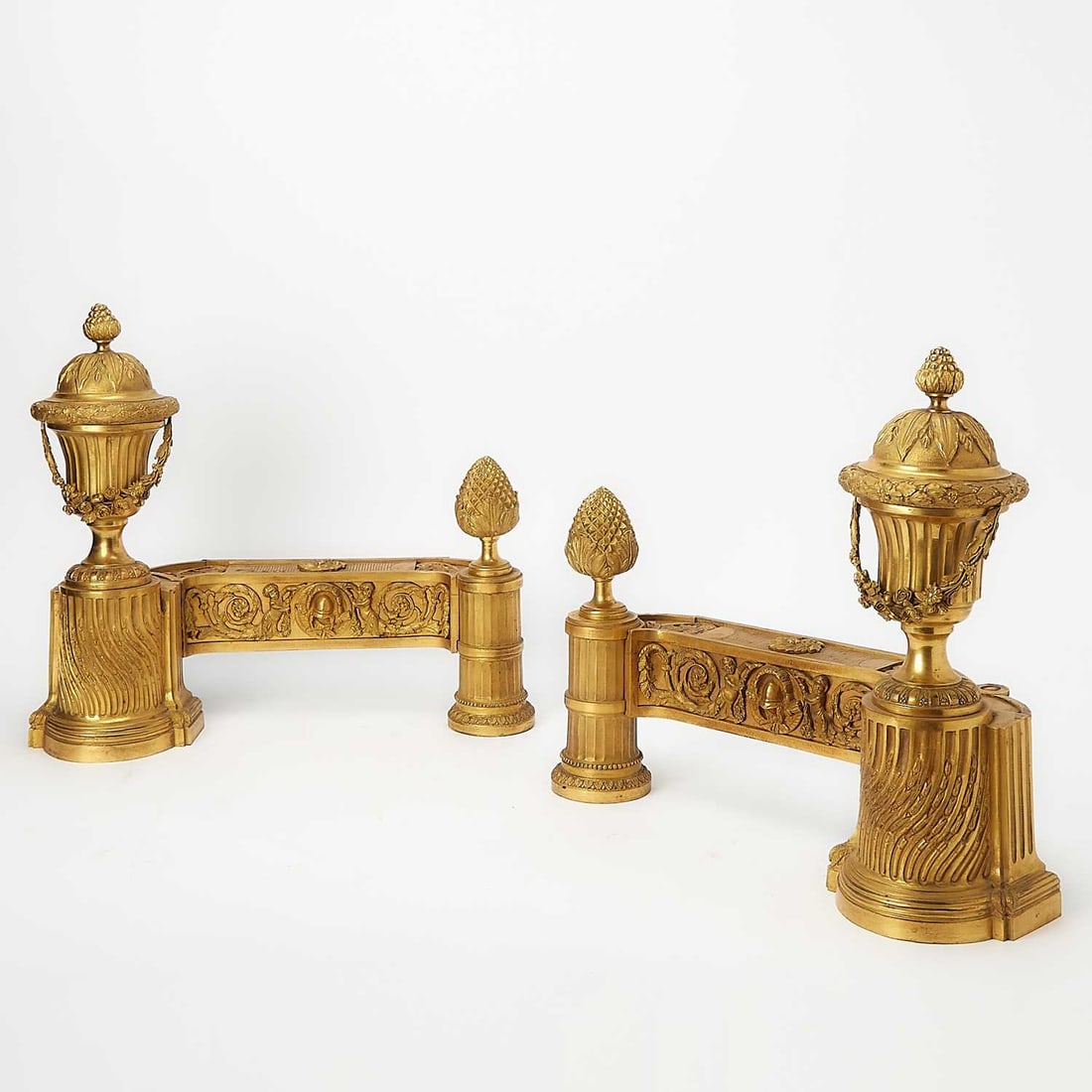 Pair of Fine Louis XVI Ormolu Chenets: Probably, circa 1780 Each surmounted by a finely cast urn-form finial with domed cover, and encircled by laurel swags and floral garland, above a fluted socle rising from a finely carved stepped base 