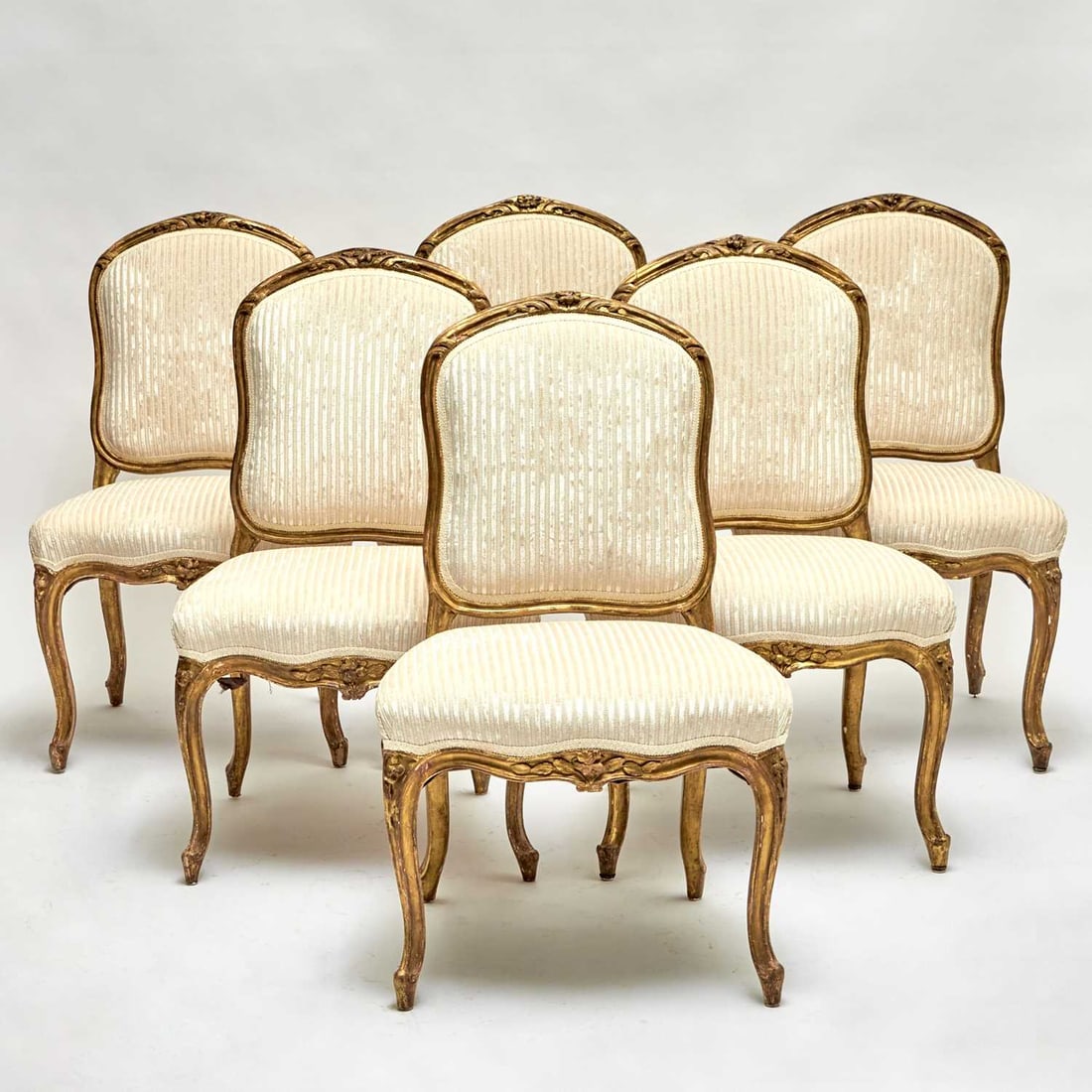 Set of Six Louis XV Carved Giltwood Chaises: Mid-18th century Each with cartouche form padded back, the crest rail centered by a carved floral spray and flanked by scrolling acanthus, the serpentine seat rail carved with rocailles and floral mot