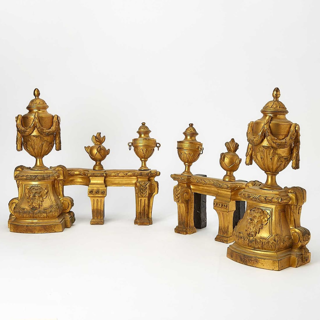 Pair of Louis XVI Style Gilt-Bronze Chenets: Circa 1770 With an urn-form finial surmounted by a foliate domed cover and acorn knop applied with draped laurel swags; the body set on a molded socle applied with a classical mask in relief; joined b