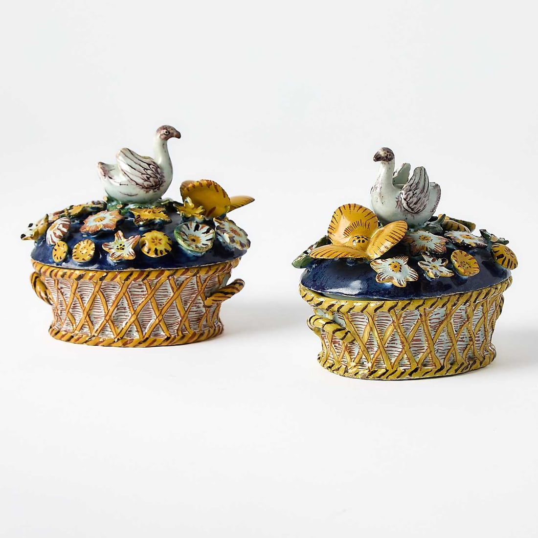 Pair of Dutch Delft Polychrome Boxes and Covers: Circa 1760 Each molded as a basket of flowers, of slightly oval form, the woven base in blue and ochre below a domed lid with applied flower blossoms on a blue ground centered by swan-form finials. He
