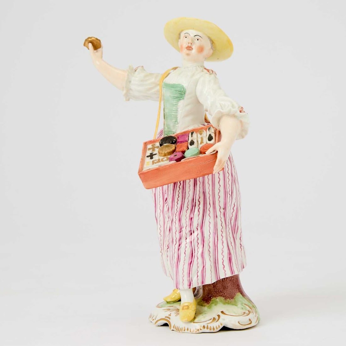 Frankenthal Porcelain Figure of a Trinket Vendor: Circa 1765, modeled by Johann Friedrich Lück The animated figure wearing a yellow-brimmed hat, turquoise bodice, and puce-striped skirt, and gilt-buckled yellow shoes, holding a snuff-box in her 