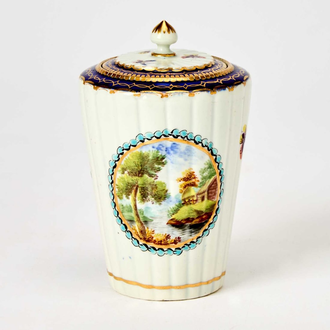 Worcester Porcelain Tea Canister and Cover: Circa 1785 Of reeded tapering cylindrical form, the center reserved with a round vignette of roses on one side and the other with a wooded landscape on a white ground with gilt borders, the top with a