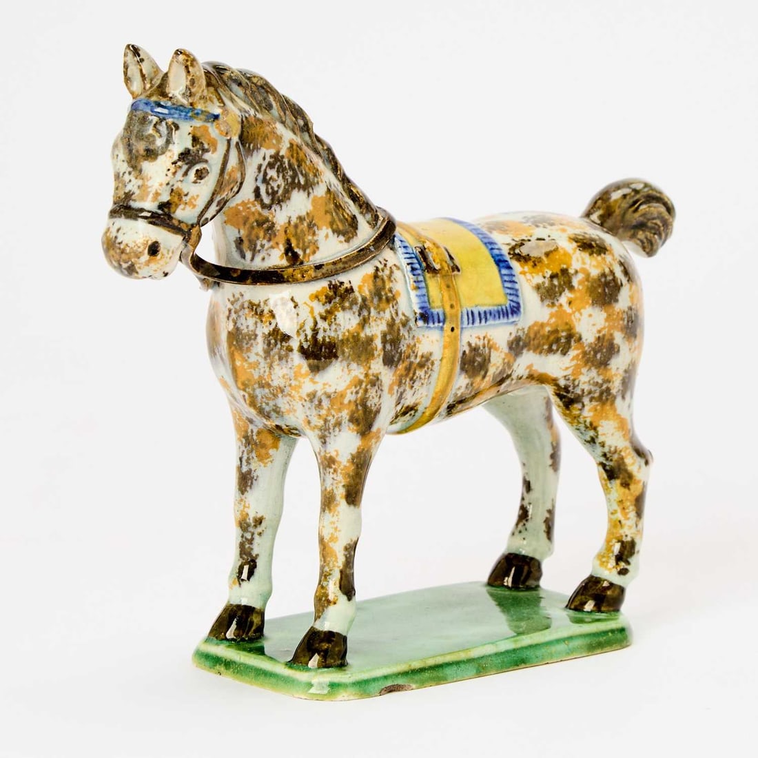 Yorkshire Pearlware Model of a Horse: Circa 1810 Of Pratt-type, realistically modeled, sponged in brown and ochre with blue-fringed yellow saddle cloth, standing on a canted rectangular green-glazed base. Height 6 1/4 inches (15.9 cm). Pr
