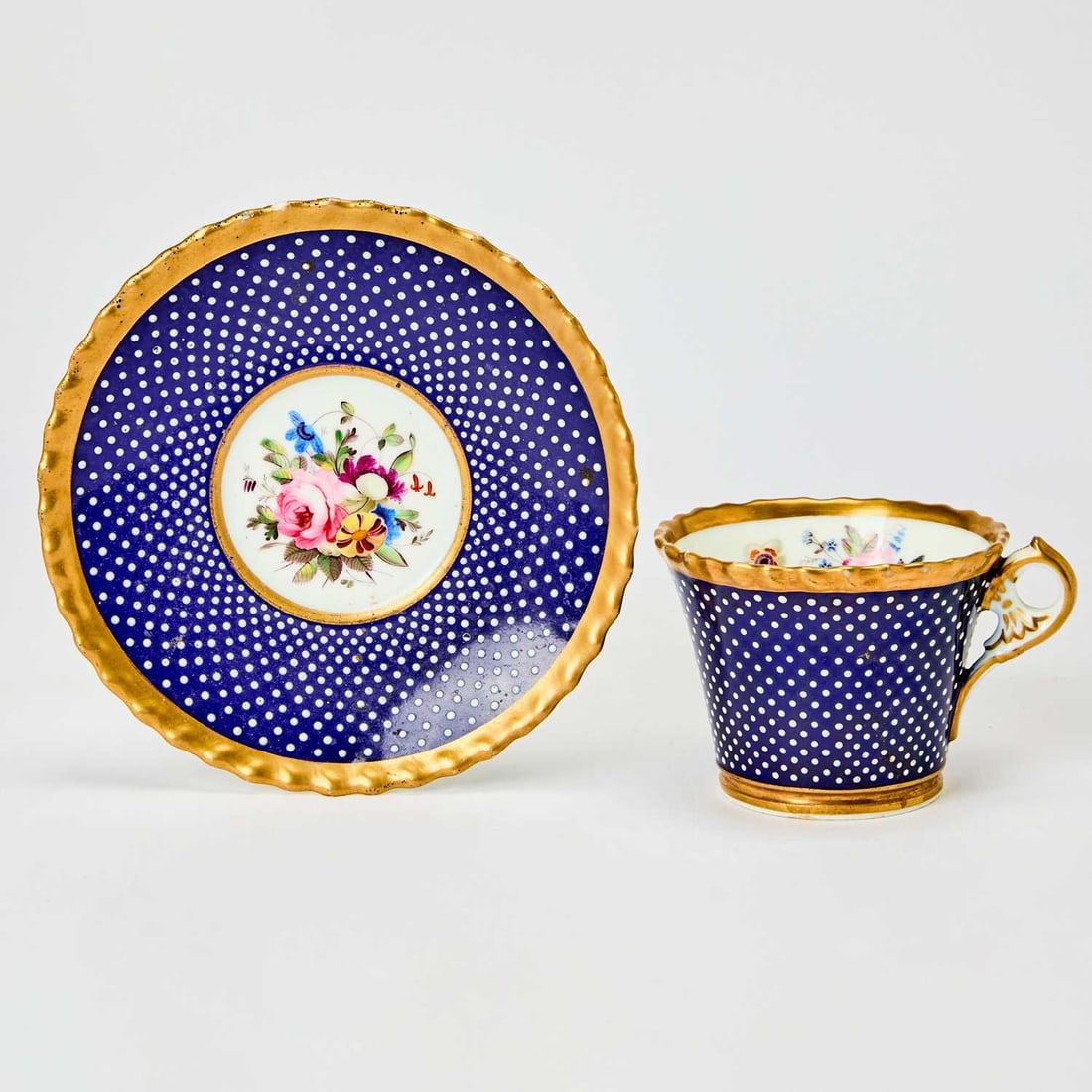 Chamberlains Worcester Porcelain Blue-Ground Jeweled Cup and Saucer: Circa 1820 With floral wreaths in bright enamels, over a blue ground, 'jeweled' overall with white bosses within a gilt scalloped border. Saucer 6 1/4 inches (15.39 cm) diameter. Overall good.