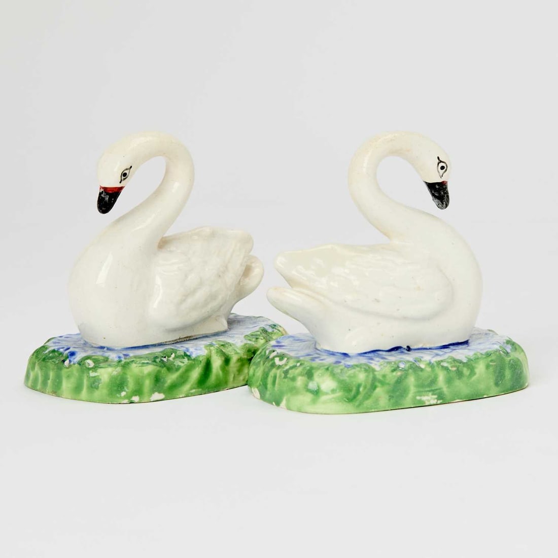 Pair of Swansea Pottery Models of Swans: Circa 1820-1840 Each realistically modeled with black eyes and beaks, the feathers incised, on oval bases modeled as ponds with blue water and green grass. Height 4 1/8 inches (10.4 cm). Provenance: S