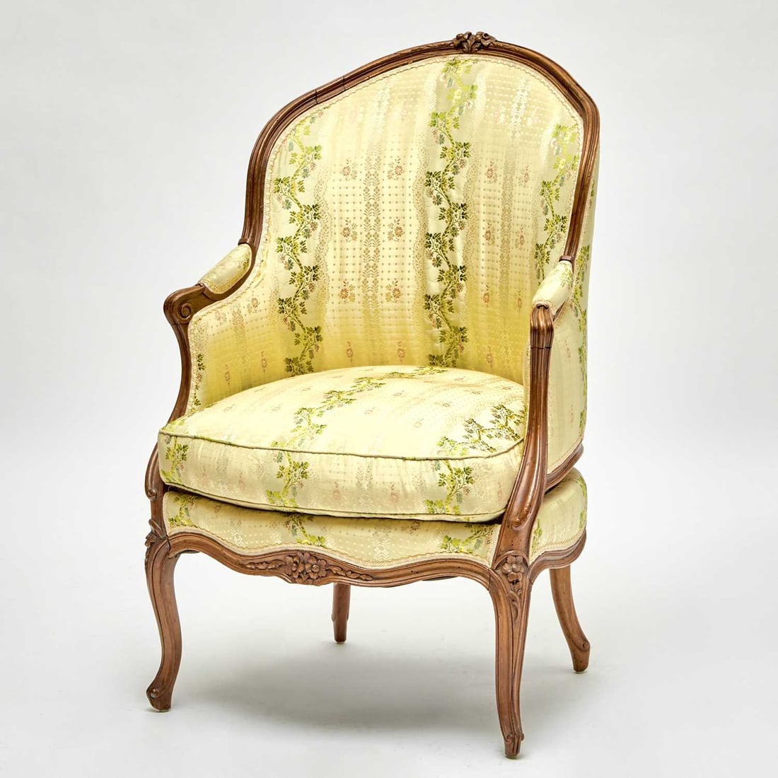 Louis XV Walnut Bergere: Mid-18th century The curved back with arched crest rail, with padded arms above a serpentine seat rail centered by a carved floral motif, on four cabriole legs, terminating in scroll feet. Height 41 1