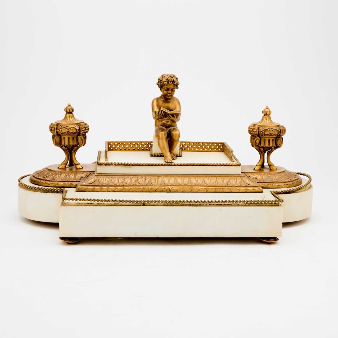 Louis XVI Style Gilt-Bronze and White Marble Inkstand: Circa 1900 The rectangular base constructed in white marble, the sides gently bowed, centered by a seated putto, depicted reading a book, set on flattened gilt-bronze feet. Height 10 1/2 inches (26.5 