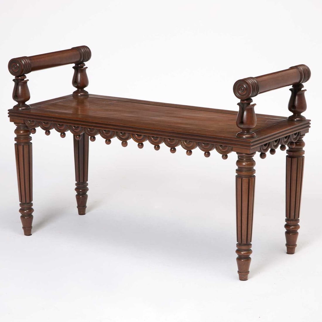 Regency Mahogany Hall Bench: Circa 1815-20, in the manner of George Bullock The molded rectangular seat below two cylindrical armrests on lotus-wrapped supports, above a three-quarter half-patarae and ball-molded apron on reeded,