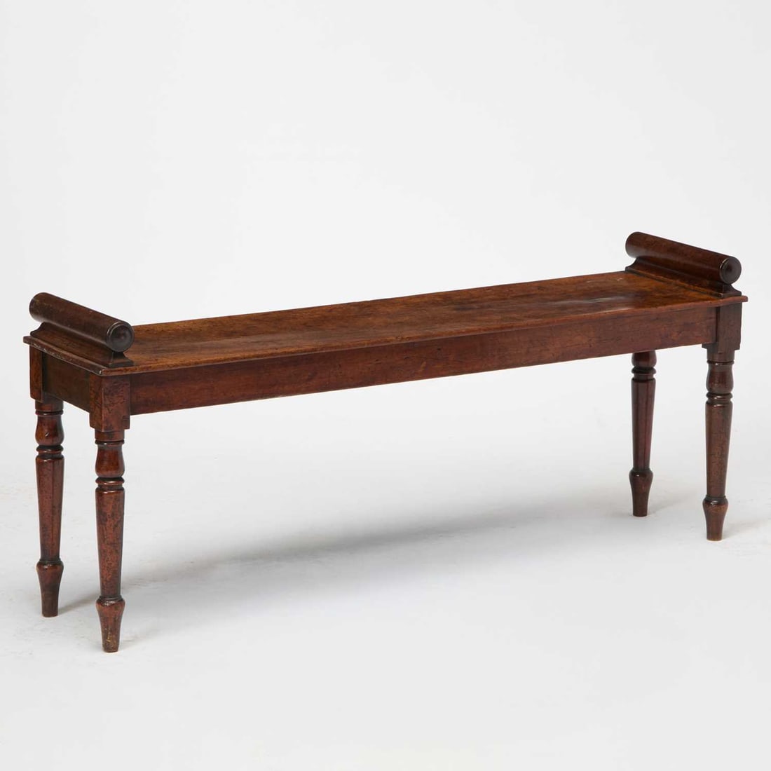 Regency Mahogany Hall Bench: First quarter 19th century The rectangular seat flanked by two scrolled ends above a plain frieze, on turned tapering legs. Height 20 1/2 inches (52 cm), width 48 inches (122 cm), depth 12 inches (30.