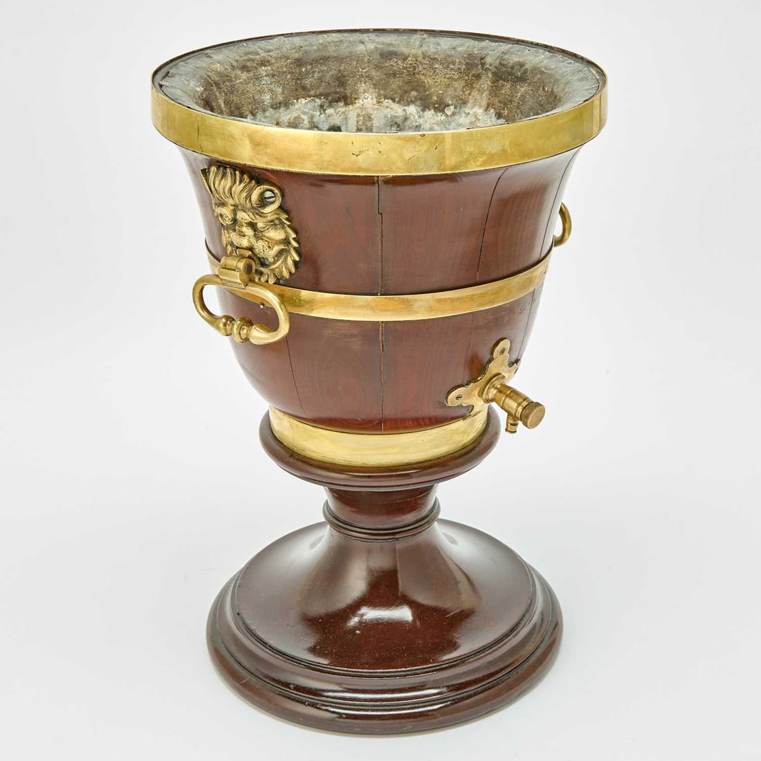William IV Brass-Mounted Mahogany Cistern: Mid 19th century Of urn form with brass lion's head and ring mask handles, on a banded socle and circular foot. Height 17 3/4 inches (75 cm), diameter 12 1/4 inches (31.1 cm).