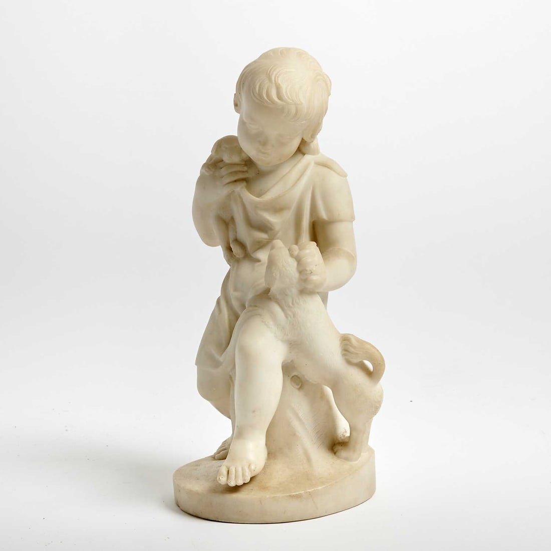English Carved Marble Figure of an Infant with Dogs: Attributed to Joseph Durham, dated 1857 Modelled as a seated child in loose classical drapery, the head gently inclined downward in a tender pose, holding a small puppy with another dog at his side, s
