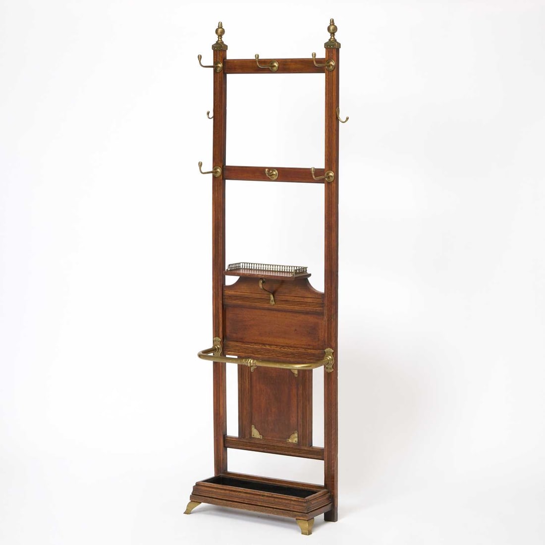 Late Victorian Brass-Mounted Walnut Hall Tree: Late 19th century, attributed to James Shoolbred & Co. With two tiers of brass hooks above a small shelf, a brass bar, and a drip pan. Height 76 inches (193 cm), width 21 3/4 inches (55.2 cm), dep