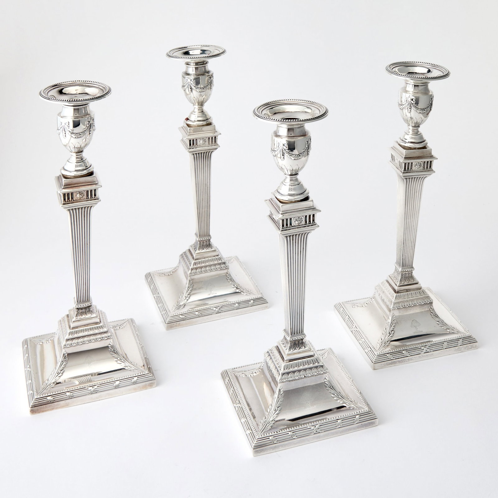 Set of Four Tiffany & Co. Sterling Silver Candlesticks: Early 20th century Each in the Adams style with fluted tapering square stem with urn-form candleholder hung with tied garland swags, on a square base with foliate corners and tied reeded border.