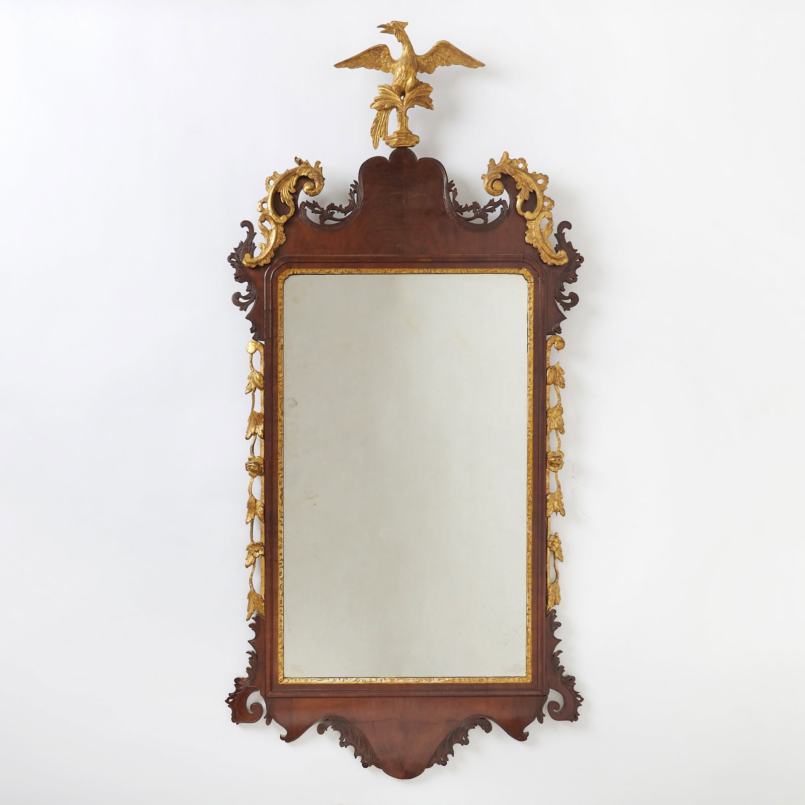 Chippendale Parcel-Gilt and Figured Mahogany Looking Glass: Probably England, circa 1755 The scrolled arched crest centering a phoenix, flanked by gilt branches of foliage. Height 56 inches, width 27 1/4 inches.