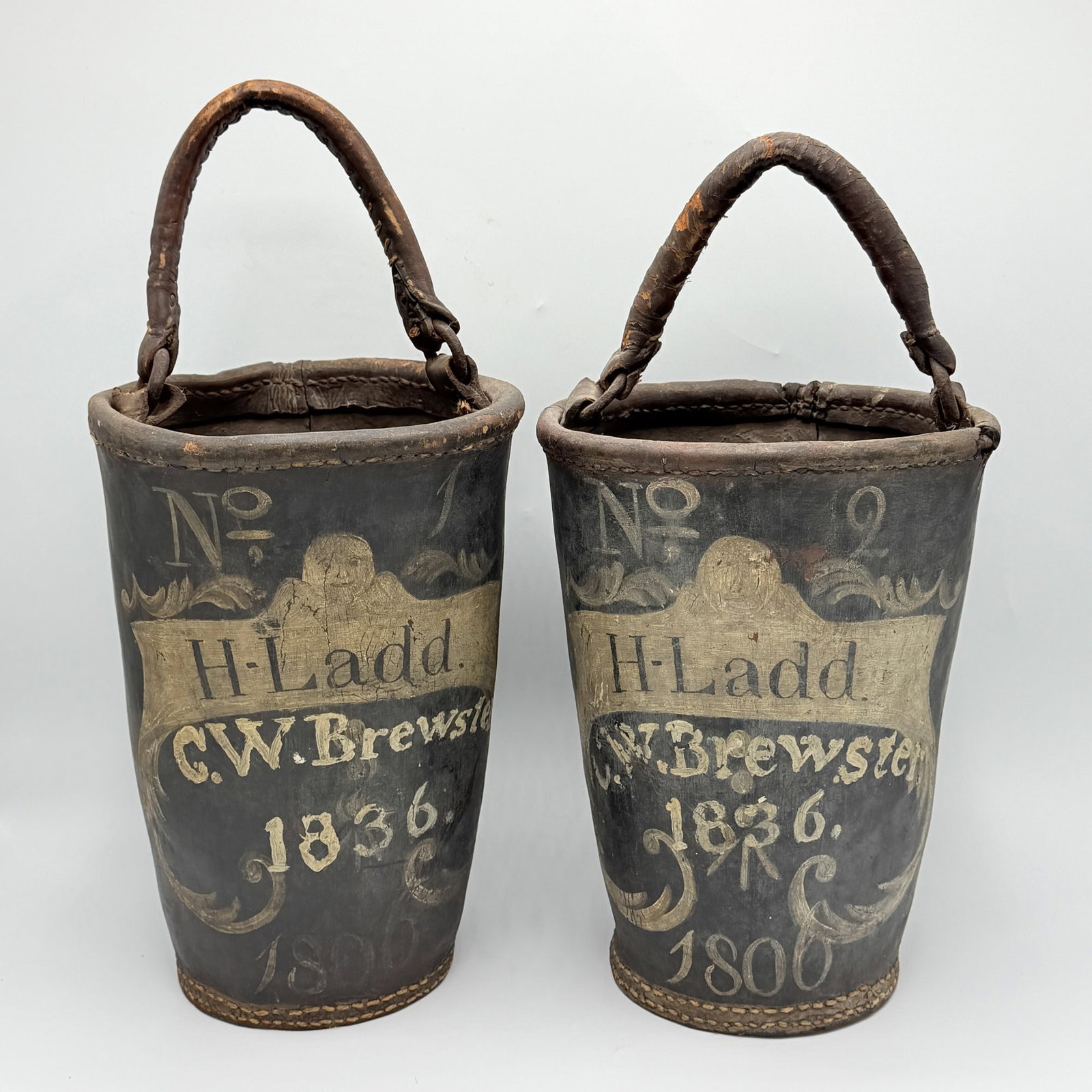 Pair of Painted Leather Fire Buckets "H. Ladd": Portsmouth, New Hampshire, circa 1806 The leather handles on iron rings above the black, red, and white-painted buckets lettered with the house residents' names. Height 11 3/4 inches Provenance: