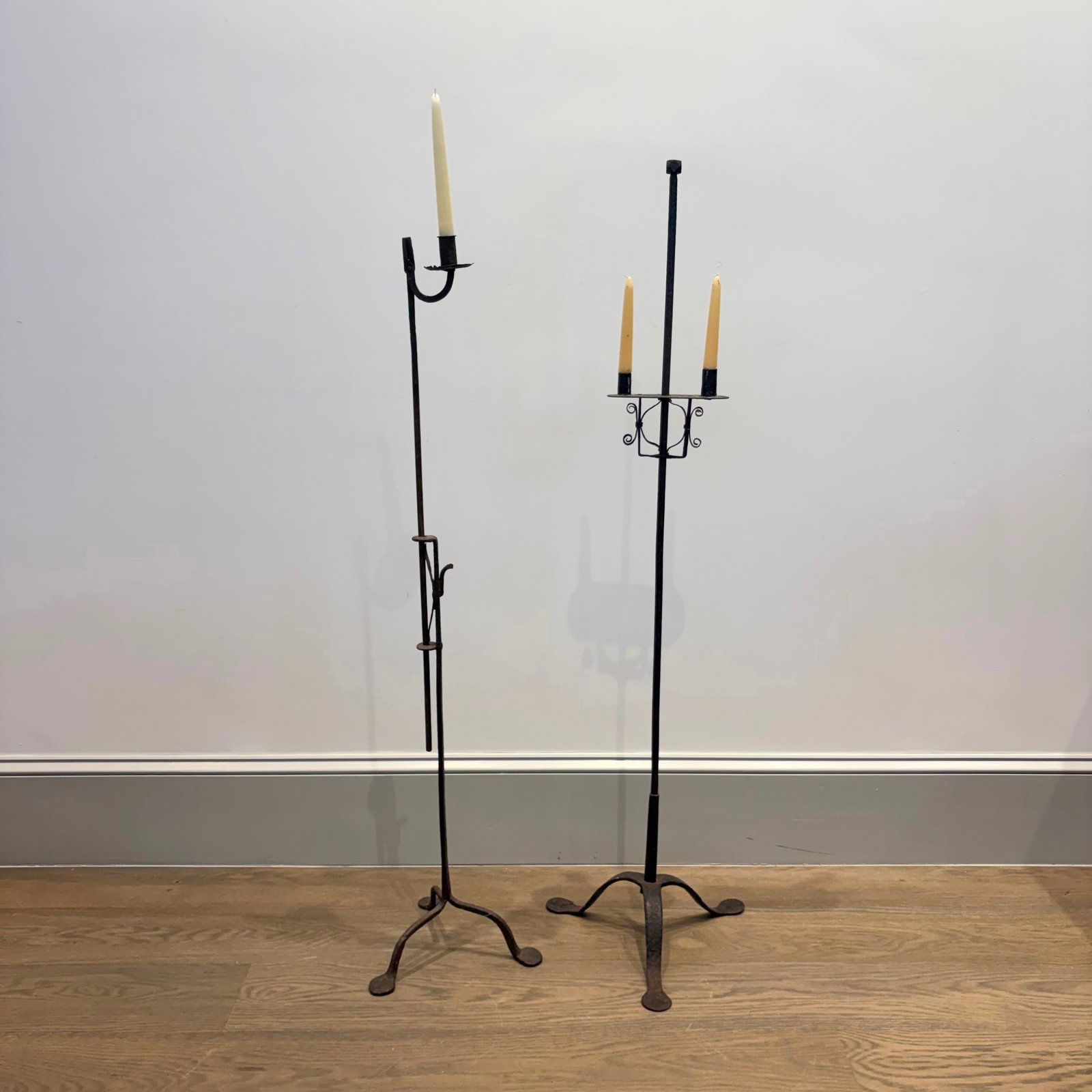 Two Wrought Iron Candlestands: America or England, 18th century Each adjustable stand on a tripod base with penny feet, one with a single candle socket, one with two. Height 50 3/4 inches.
