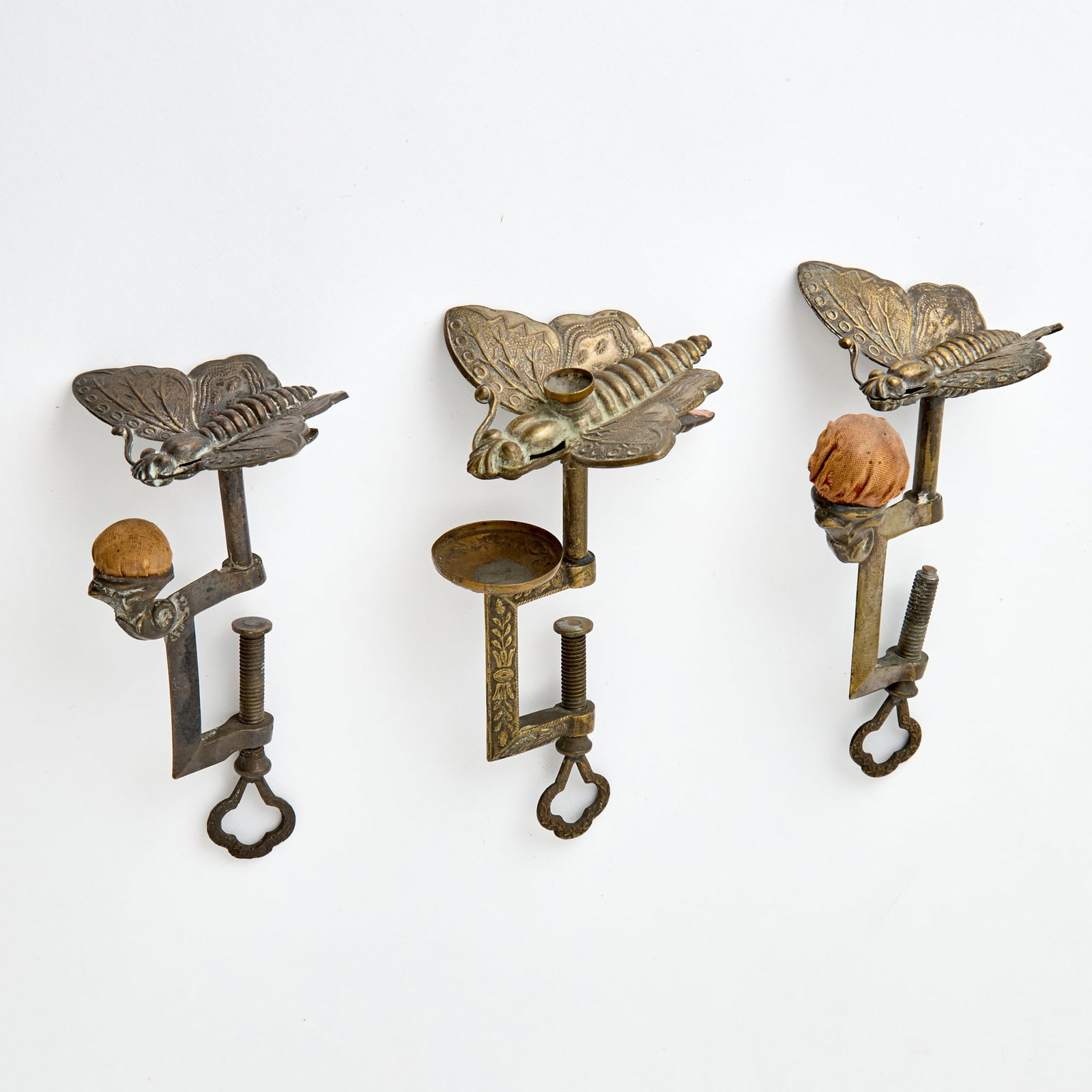 Three Silvered Metal and Brass Butterfly Sewing Clamps with Pin Cushions: Mid 19th century Two bearing stamps PATENTED Nov 8th 1853. Height of largest 5 1/4 inches.