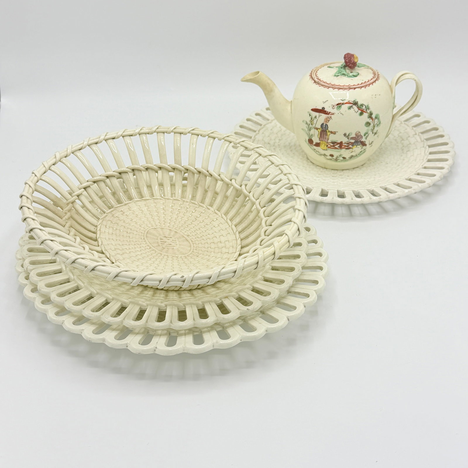 Five Pieces of English Creamware: Late 18th century Comprising a Wedgwood plate and two small oval platters, each with pierced loop rims, a fruit basket, and a round teapot with Chinoiserie decoration. Length of longest platter 11
