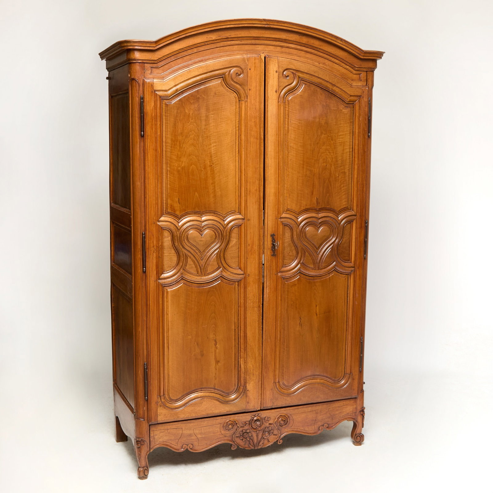 Louis XIV Provincial Walnut Armoire: 18th century and later The arched top surmounting two carved and molded panel doors, centered by hearts enclosing shelves above a shaped apron centered by floral sprigs, on cabriole legs and scroll fe