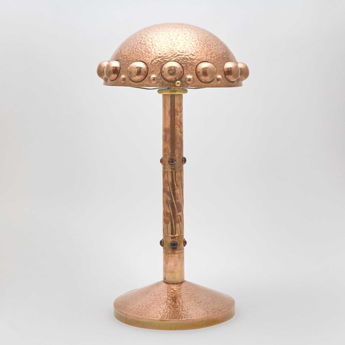 Austrian Secessionist Hand-Hammered Brass and Glass Cabochon-Set Table Lamp: Vienna, circa 1910-20 The domed shade raised on a columnar standard, inset with ruby red colored cabochons, ending in a domed circular foot, unsigned. Height 22 inches, diameter of shade 10 inches.