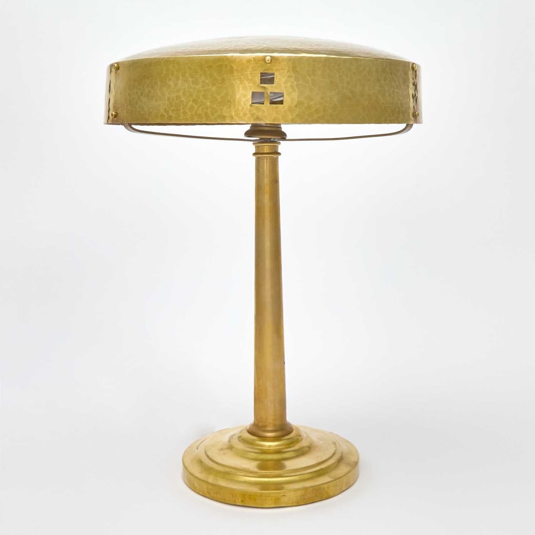 Secessionist Hammered Brass Table Lamp: Circa 1910 The short domed shade with pierced square cutouts, rivets and a hand-hammered finish, raised on a plain columnar stem ending is a stepped circular foot, unsigned. Height 15 1/4 inches; heig