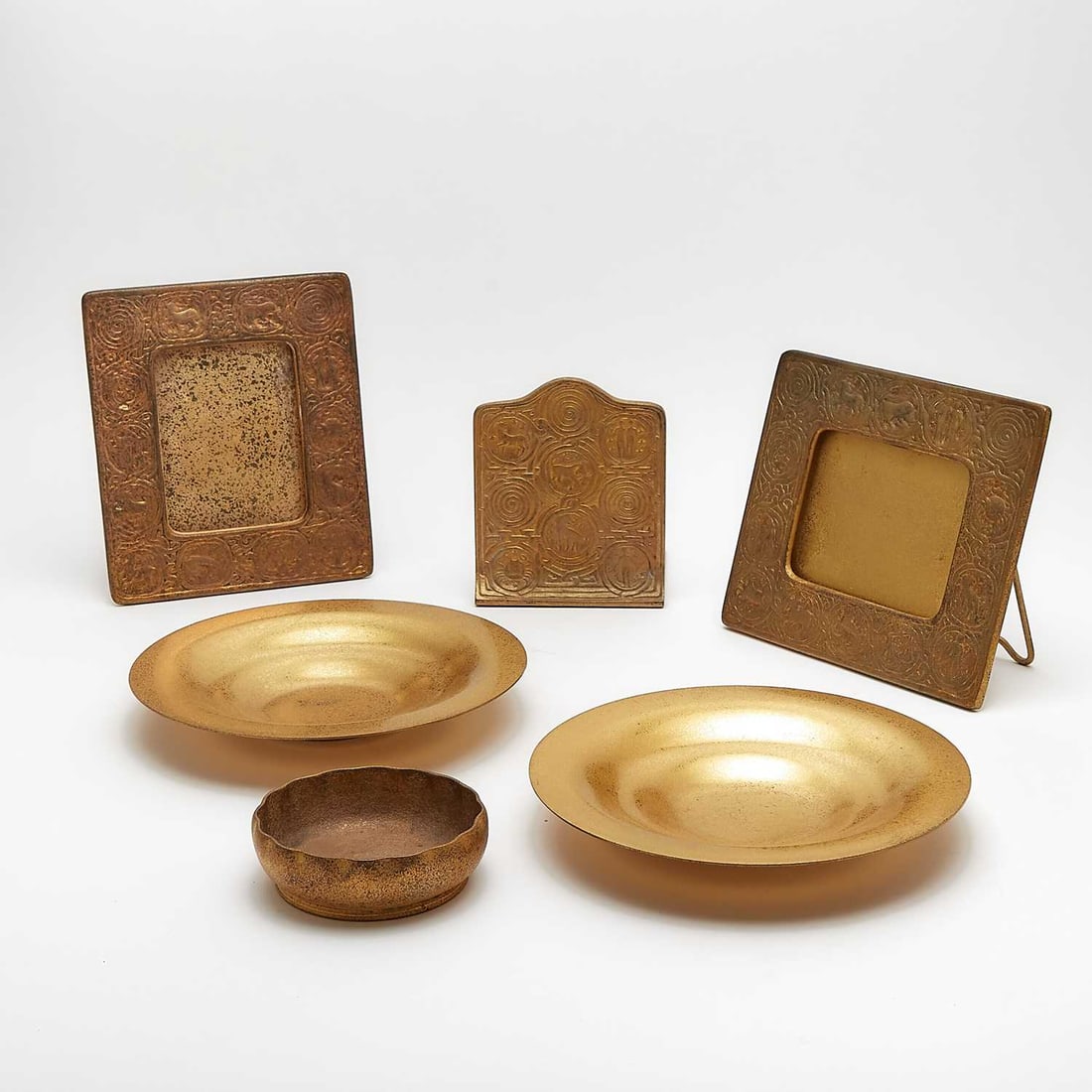 Group of Tiffany Studios Gilt-Bronze Desk Articles: Comprising a photograph frame, calendar frame and a single bookend, in the Zodiac patterns, each stamped TIFFANY STUDIOS NEW YORK and numbered, height of tallest 8 1/8 inches, width 7 1/8 inches; two 