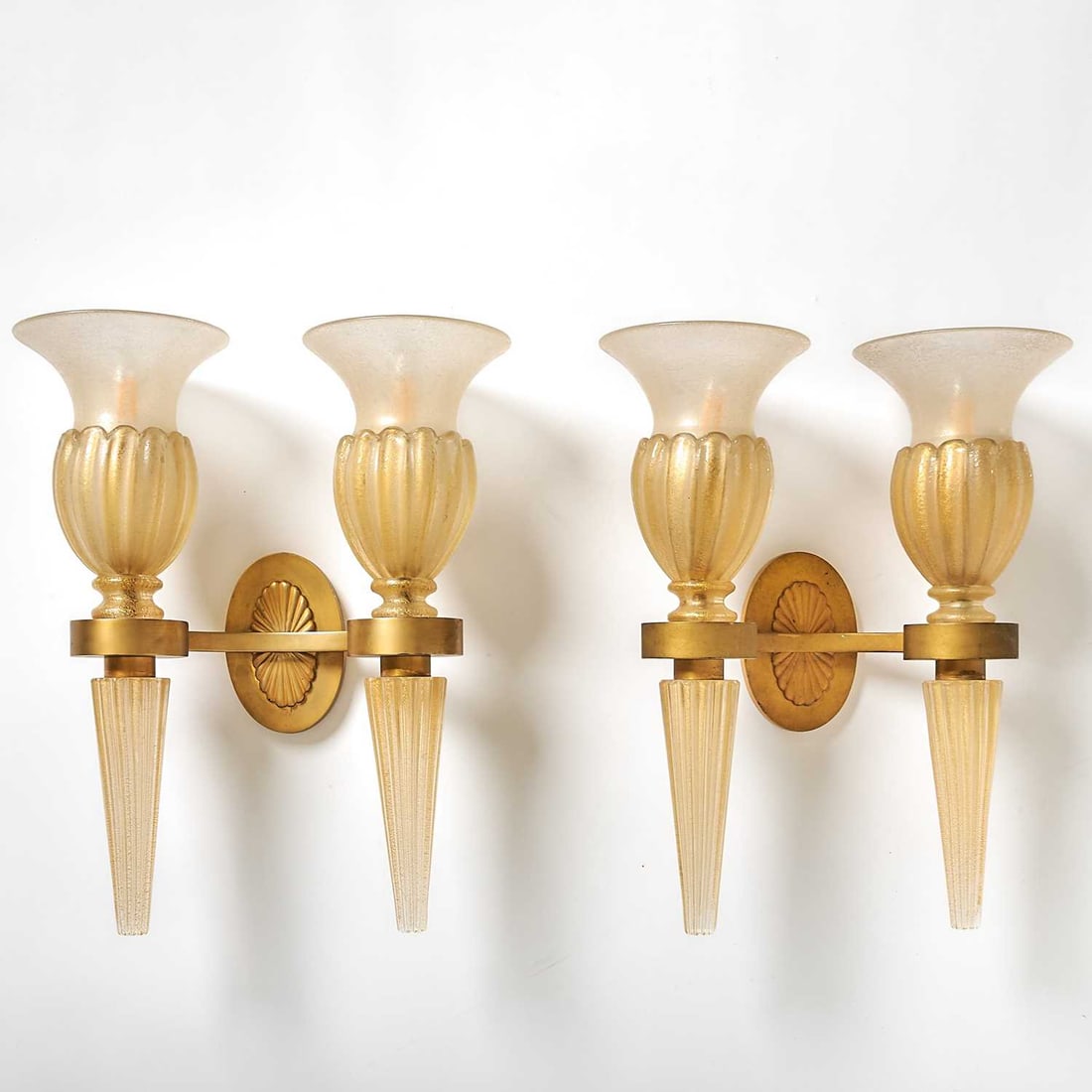 Pair of Seguso Murano Hand-Blown Glass and Gilt-Metal Two-Light Wall Sconces: Second half 20th century Each with an oval backplate fronted by a curved support issuing a pair of two-part ribbed torch-form shades, in colorless glass, internally decorated with gold foil flecks. He