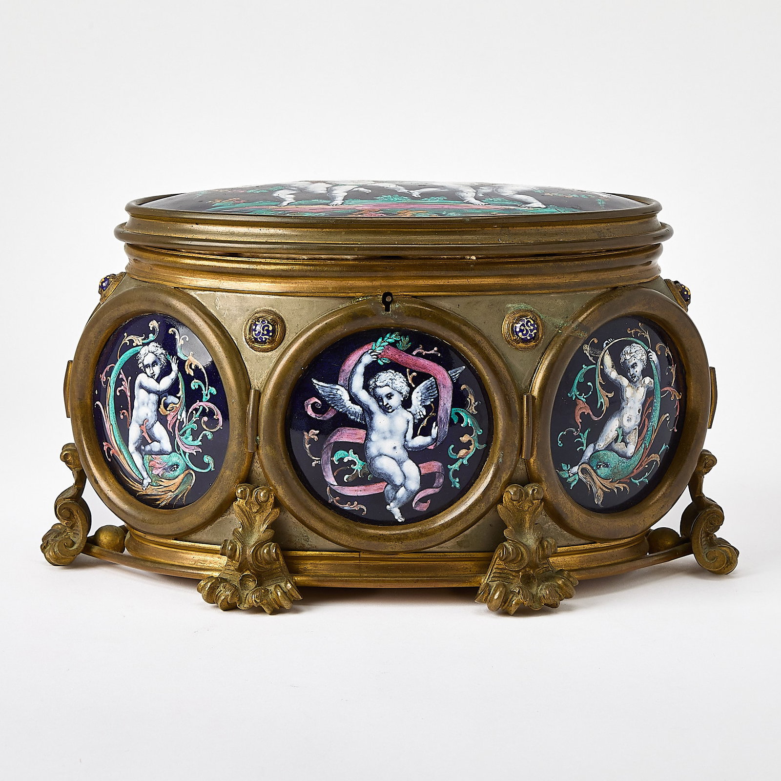 Limoges Enamel Jewel Casket: Early 20th century The hinged oval lid mounted with a panel of dancing putto above a conforming case, the interior lined with tufted purple silk, the exterior further with roundels of putti, on acanth