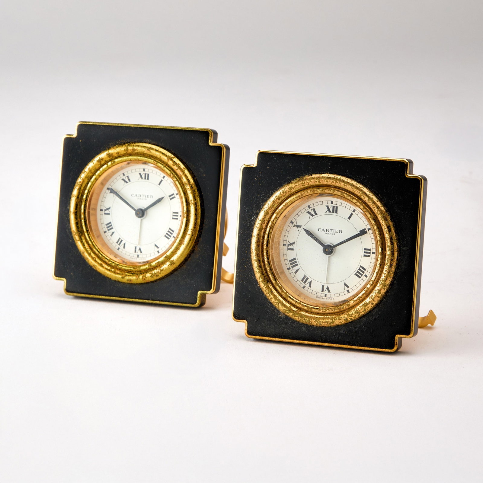 Pair of Cartier Gilt Metal and Black Enamel Travel Clocks: Model 7512. Each in a fitted case. Height 3 inches. Enamel and gilding on front distressed