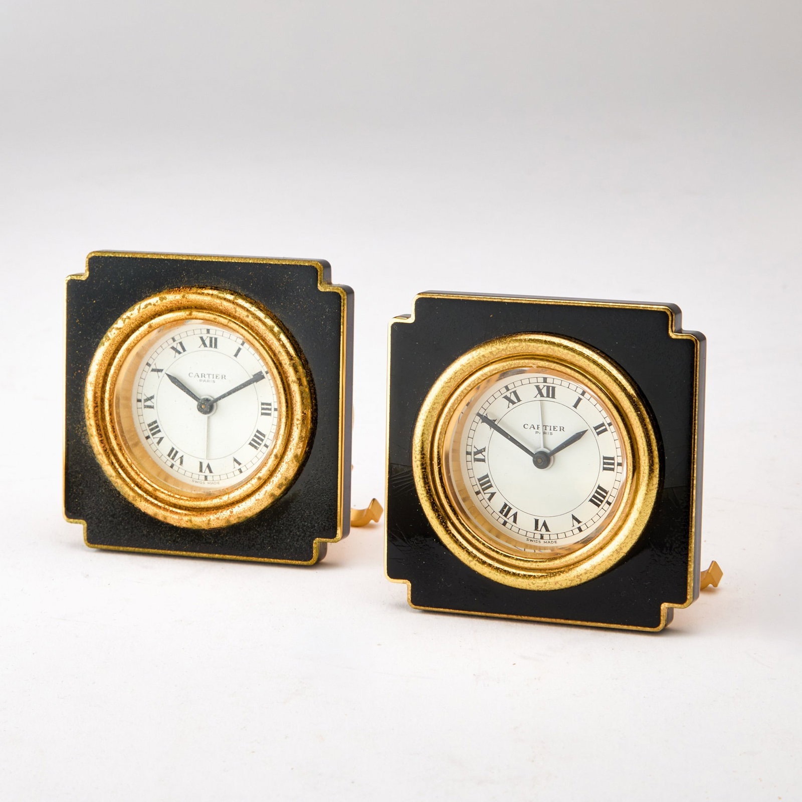 Pair of Cartier Gilt Metal and Black Enamel Travel Clocks: Model 7512. Each in a fitted case. Height 3 inches. Enamel and gilding on front distressed
