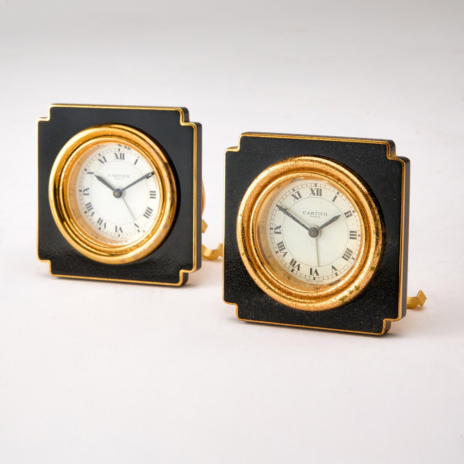 Pair of Cartier Gilt Metal and Black Enamel Travel Clocks: Model 7512. Each in a fitted case. Height 3 inches. Enamel and gilding on front distressed