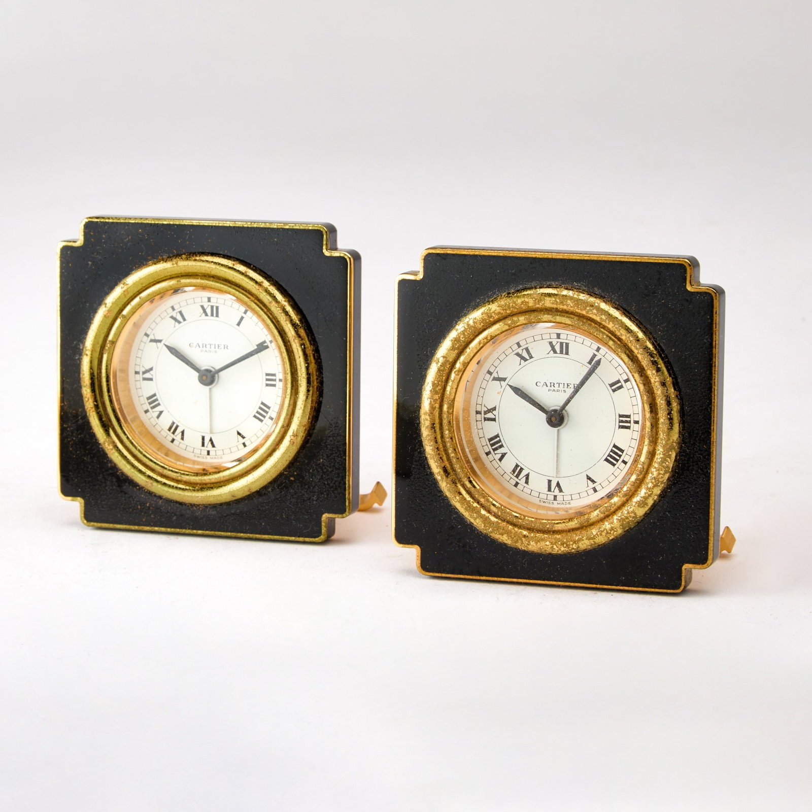 Pair of Cartier Gilt Metal and Black Enamel Travel Clocks: Model 7512. Each in a fitted case. Height 3 inches. Enamel and gilding on front distressed