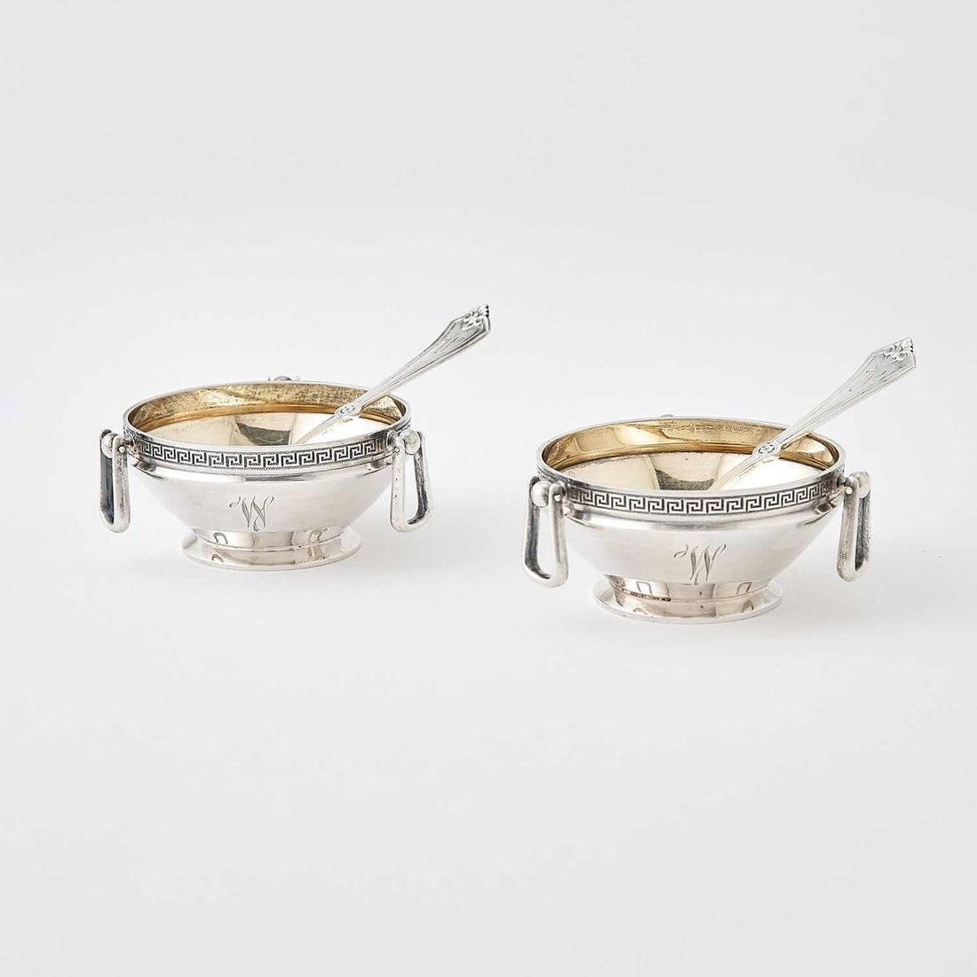 Pair of Gorham Sterling Silver Open Salts: 1860s Each circular with greek key border and hung with three loose ring handles; with a pair of sterling silver salt spoons. Diameter 2 3/4 inches, total approximately 4 ounces. Generally good condit