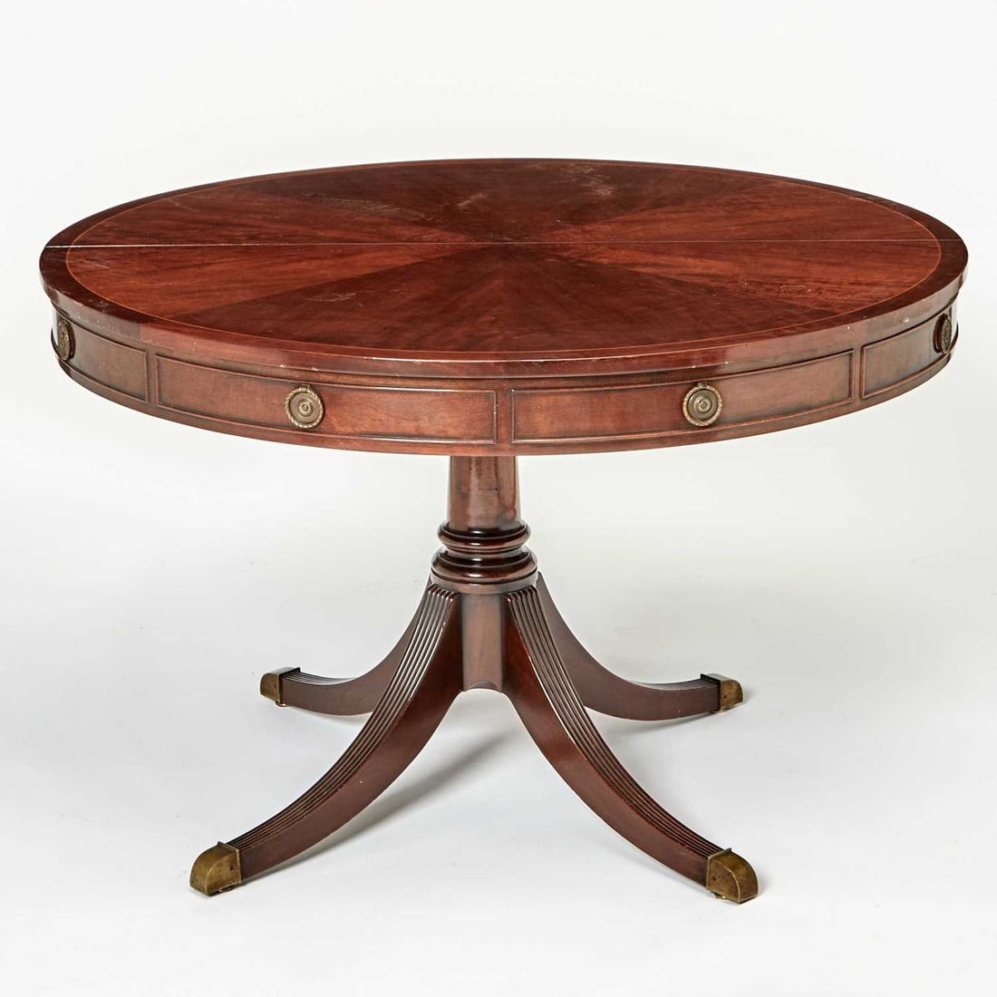 Regency Style Inlaid Mahogany Circular Extension Pedestal Dining Table: Late 20th century The top veneered in a sunburst pattern, with an apron and brass handles to look like a library table; with one additional leaf. Height 29 inches, diameter 48 inches, leaf width 24 in