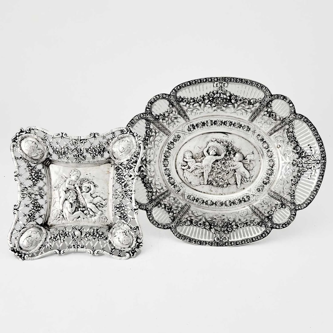 Two Continental Silver Dishes: Late 19th/early 20th century One oval, the other square, each with pierced borders, the centers chased with scenes of putti. Lengths 8 1/2 inches and 14 1/4 inches, total approximately 24 ounces.
