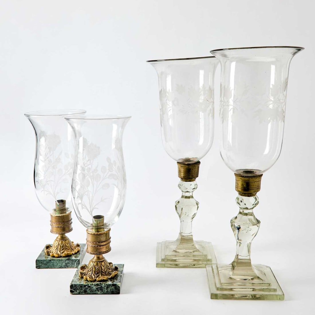 Two Pairs of Etched Glass Photophores: Comprising a tall pair with a brass-mounted base with a faceted knopped and baluster-form stem, ending in a stepped square foot, and a shorter pair with metal mounts, ending in a square green marble f