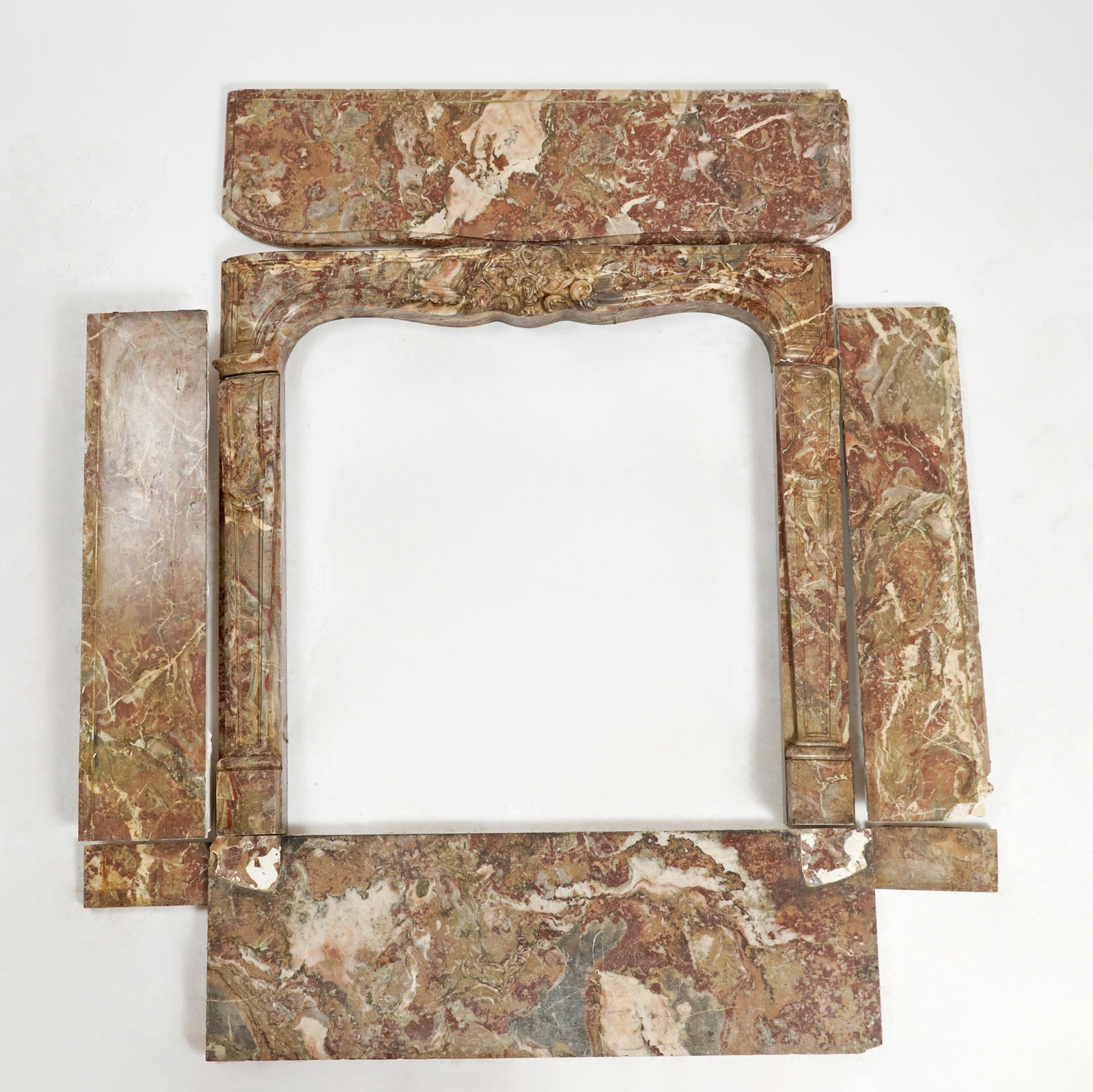 Louis XV Rouge Marble Fireplace Mantel: Third quarter 18th Century, Finely carved in a variegated Breccia marble, the serpentine top over a frieze centered by a cartouche of scrolling rocaille ornament, with conforming fluted jambs terminat