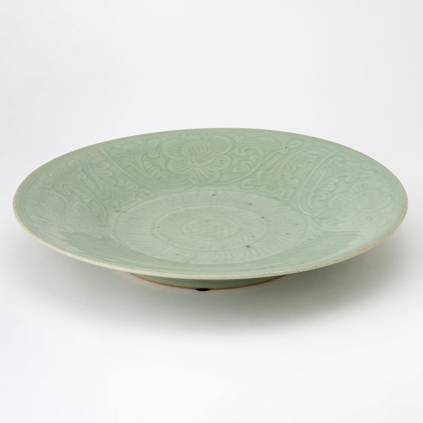 Chinese Celadon Glazed Carved Porcelain Charger Qing Dynasty: Of shallow circular form, the interior decorated with a central medallion surrounded by blossoms and scrolling foliage. (Diameter 14 1/2 inches)