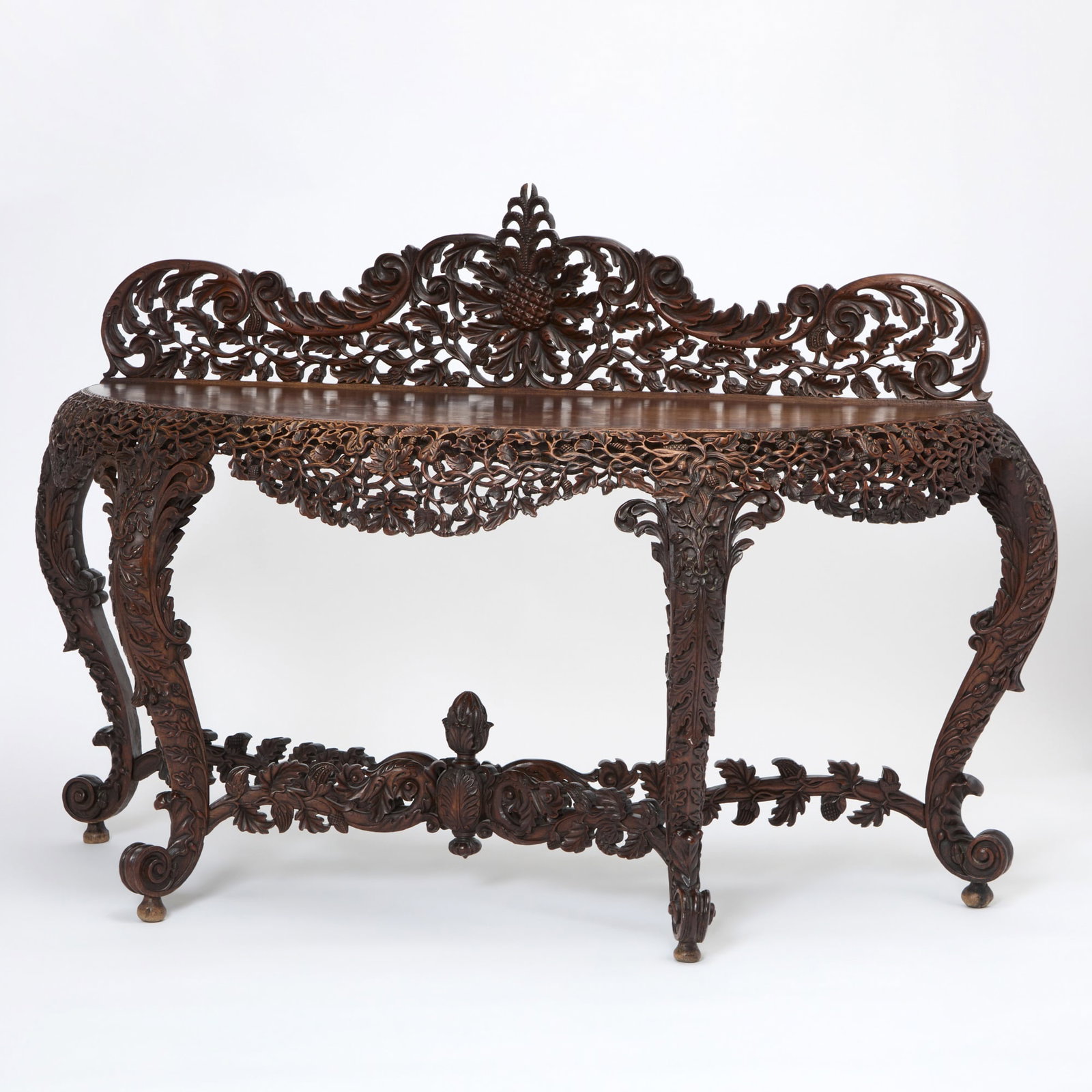 Anglo-Indian Hardwood Console: Late 19th century Of demilune form with a shaped backsplash, pierced and carved throughout with scrolling foliage, raised on cabriole legs joined by an X-stretcher and ending in scroll feet. Height