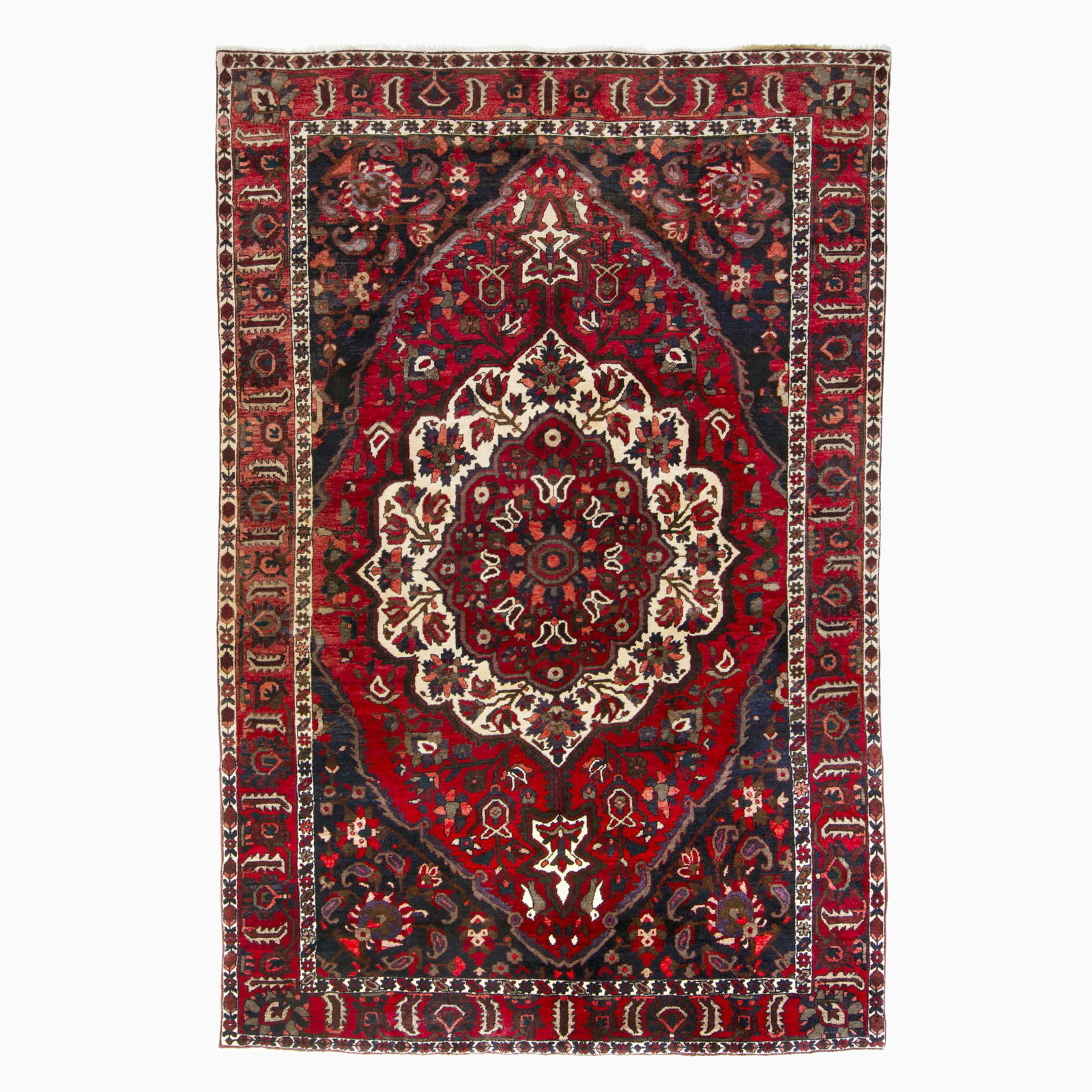 Bakhtiari Carpet: South Iran, Late 20th century The central circular pendant medallion on the crimson field flanked by indigo spandrels is within a palmette and leaf border. (10' 0" x 6' 8") Minor color runs, faint
