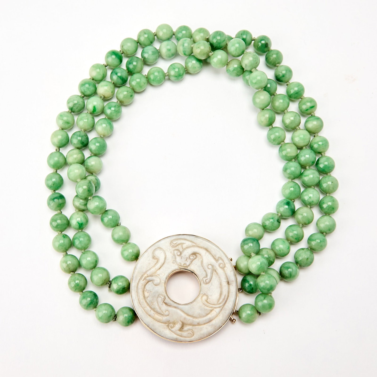 A Chinese Jadeite-Bead Necklace with a Carved White Jade Bi Pendant Bi Ming Dynasty or Earlier: The triple-strand necklace suspending a jade bi disc carved in relief with an encircling chilong and fitted with a 14k gold mount. (Diameter of bi disc 2 inches; length of necklace 9 1/4 inches)